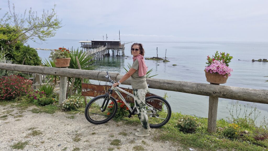 una donna in bicicletta con panorama marittimo sullo sfondo un trabocco